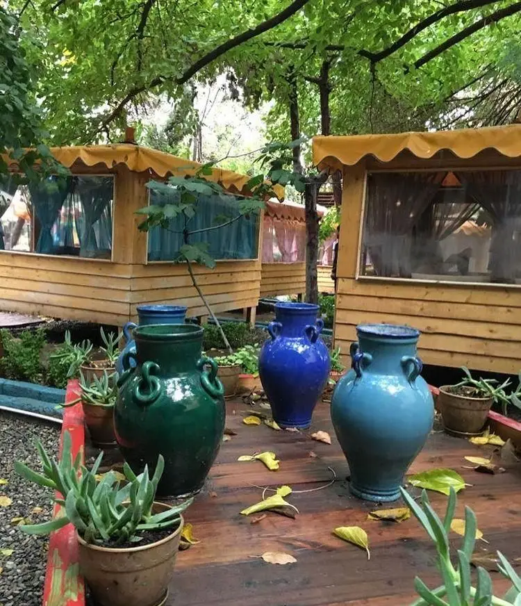 رستوران باغ لاله با فضای باز دلنشین، آلاچیق‌های چوبی زیر درختان سرسبز و گلدان‌های تزئینی رنگارنگ، مکانی آرامش‌بخش برای مشتریان.