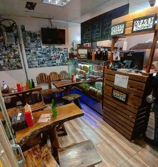 فضای داخلی گرم و صمیمی ساندویچی مقدم در تهران، با میز و صندلی‌های چوبی دست‌ساز، پیشخوان نمایش غذاها و نوشیدنی‌ها، مناسب فست فود.