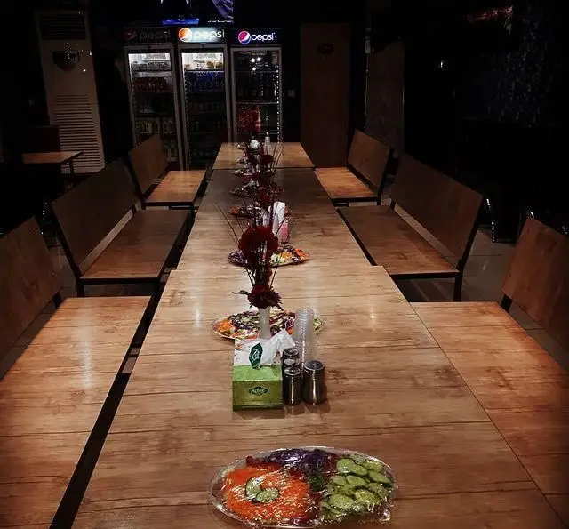 فضای داخلی کبابسرای ریحون با میزهای چوبی بلند و نیمکت‌های راحت برای مشتریان، آماده پذیرایی در محیطی دلنشین و دنج.