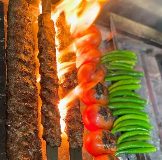سیخ‌های بلند کباب کوبیده گوشت، گوجه فرنگی و فلفل سبز تند در حال گریل شدن روی آتش داغ. طعم اصیل غذای تازه در فلافل کیلویی میخکوب.