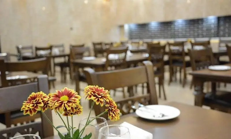 فضای داخلی دلنشین و چیدمان زیبای میز و صندلی‌های چوبی رستوران عمارت با گل‌آرایی روی میزها، آماده پذیرایی.