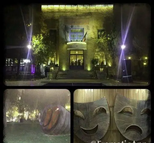 نمای شب خانه هنرمندان ایران با نورپردازی دلنشین، ورودی اصلی، فضای سبز و آثار هنری شامل مجسمه و ماسک‌های تئاتر.