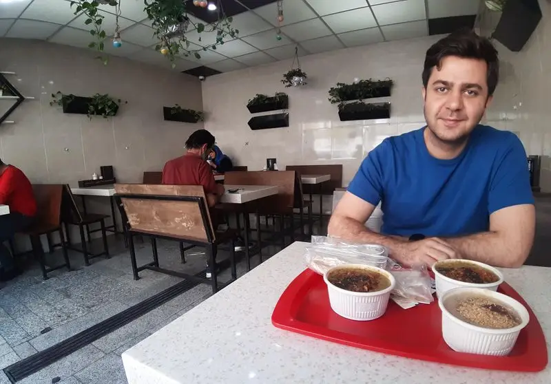 یک مشتری شاد در رستوران آش و حلیم دارچین، با سه کاسه حلیم خوش طعم و داغ برای صبحانه روی میز.