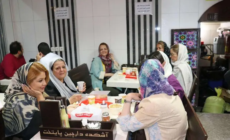 مشتریان شاد در آشکده دارچین پایتخت تهران. گروهی از زنان و مردان در حال لذت بردن از آش و حلیم داغ و خوشمزه.