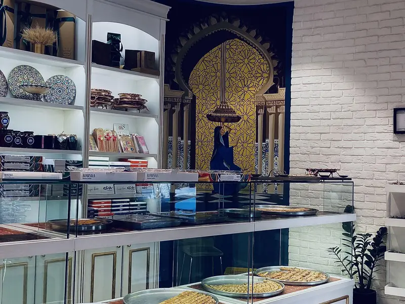 فروشگاه شیرینی لبنانی روشه با دکوراسیون داخلی سنتی و مدرن، نمایش سینی‌های باقلوا و انواع شیرینی‌های لذیذ در ویترین شیشه‌ای.