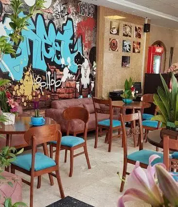 فضای داخلی دنج و هنری کافی شاپ پالمیرا با دیوارگرافیتی مدرن، مبلمان راحتی و میز و صندلی چوبی برای تجربه‌ای دلنشین.