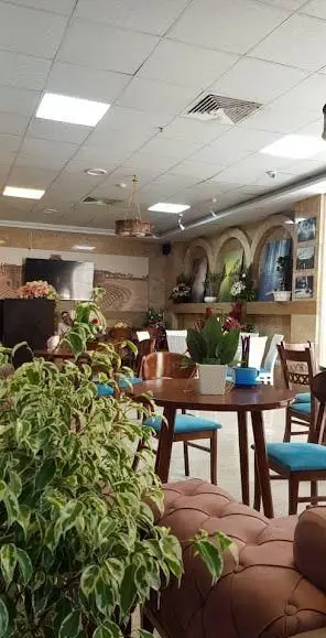 فضای داخلی لوکس و دنج کافی شاپ پالمیرا با میزهای چوبی، صندلی‌های آبی، مبلمان راحتی قهوه‌ای و گلدان‌های گیاه سبز زیبا.