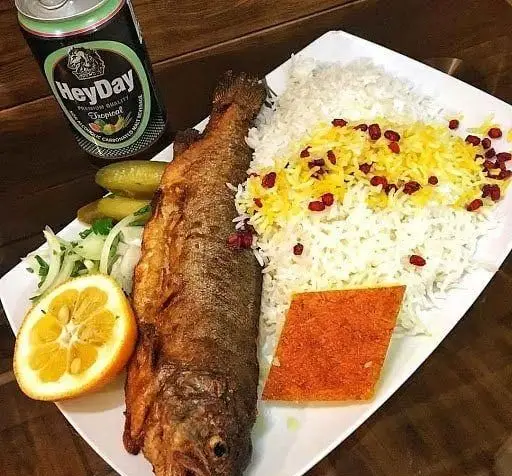 وعده غذایی لذیذ ماهی سرخ شده با پلو زعفرانی و زرشک در رستوران طهورا. شامل خیارشور، سالاد، برش پرتقال و نوشابه HeyDay.