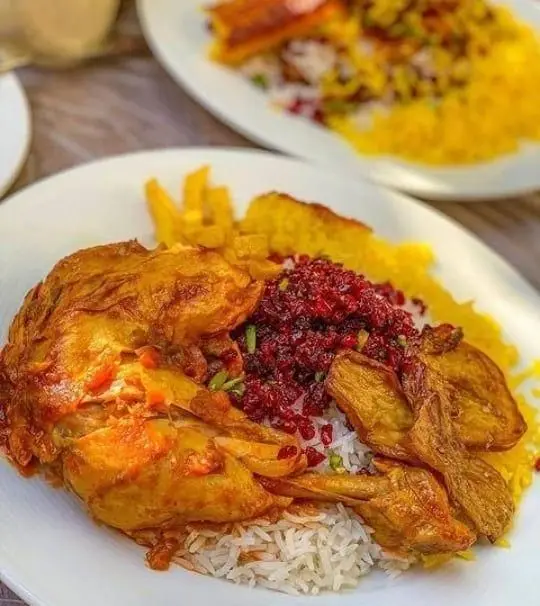 غذای خوش طعم رستوران طهورا شامل مرغ مجلسی با زرشک پلو و برنج زعفرانی، سیب زمینی سرخ کرده و ته دیگ، یک غذای سنتی ایرانی.