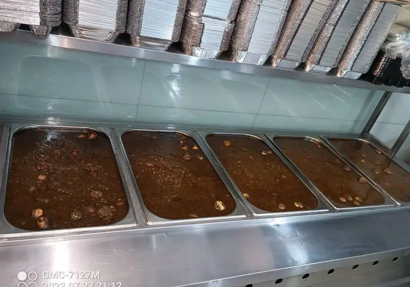 سینی‌های بزرگ از خورشت آماده و لذیذ در آشپزخانه تهیه غذای شرکتی پارسی آنیسا شعبه یادگار، به همراه ظروف آلومینیومی برای بسته‌بندی.