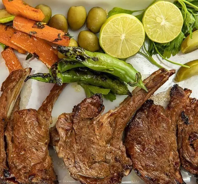 تصویری از شیشلیک دنده گوسفندی کبابی با مخلفات تازه شامل هویج، فلفل، زیتون و لیمو در رستوران بین المللی ۱۳۳.