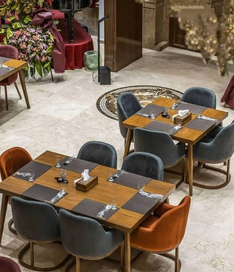 رستوران بین المللی ۱۳۳: فضای داخلی دلباز با میز و صندلی‌های مدرن در رنگ‌های خاکستری و نارنجی، کفپوش مرمر و تزئینات گل زیبا.