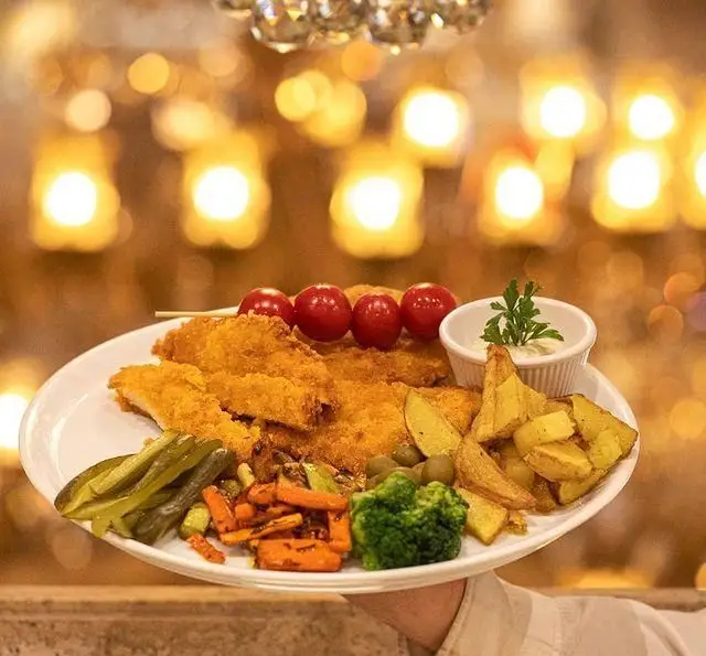 غذای خوشمزه در رستوران بین المللی ۱۳۳ شامل شنیسل مرغ ترد، سیب زمینی، انواع سبزیجات تازه، خیارشور و زیتون با سس ویژه و گوجه گیلاسی.