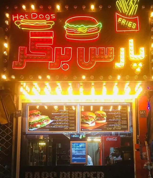 نمای شب فست فود پارس برگر با تابلوهای نئونی Hot Dogs، Burger، Fries و نام پارس برگر، همراه با منوی متنوع و روشن.