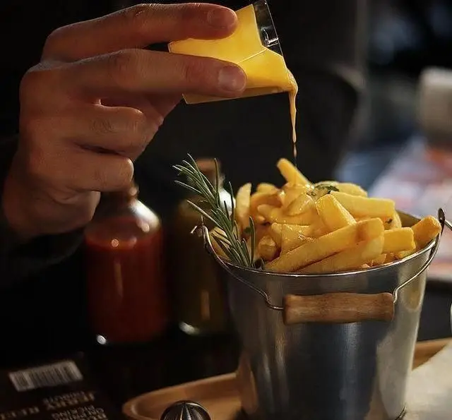 سس پنیر لذیذ در حال ریختن بر روی سیب زمینی سرخ کرده طلایی در کافه رستوران پاشا. فرنچ فرایز با سس پنیر، تجربه‌ای خوشمزه از فست فود.
