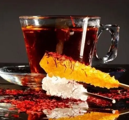 چای زعفرانی غلیظ با نبات کریستالی زعفرانی و سفید روی میز کافه رستوران پاشا، نشان‌دهنده طعم اصیل و کیفیت برتر نوشیدنی‌ها.