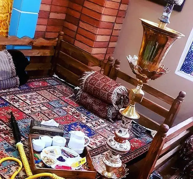 نمایی زیبا از فضای سنتی و دلنشین کافه رستوران پاشا با دکوراسیون گرم، قلیان، فرش‌های اصیل، پشتی‌های راحت و سینی چای و میان‌وعده آماده پذیرایی.