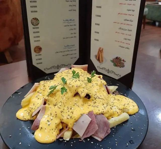 سیب زمینی سرخ کرده با برش‌های ژامبون و سس پنیر فراوان در کافه رستوران پاشا، یک انتخاب عالی از منوی غذاهای خاص.