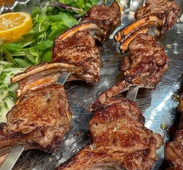 تصویری جذاب از کباب دنده و شیشلیک گوشت بره تازه و لذیذ، با سیخ در کافه رستوران پاشا. غذای سنتی ایرانی سرو شده با سبزیجات معطر و برش لیمو تازه.