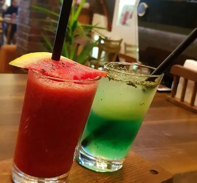 تصویری جذاب از دو نوشیدنی تابستانی: اسموتی هندوانه قرمز و کوکتل سبز لایه‌دار، آماده سرو در کافه رستوران پاشا. حس طراوت و تازگی.