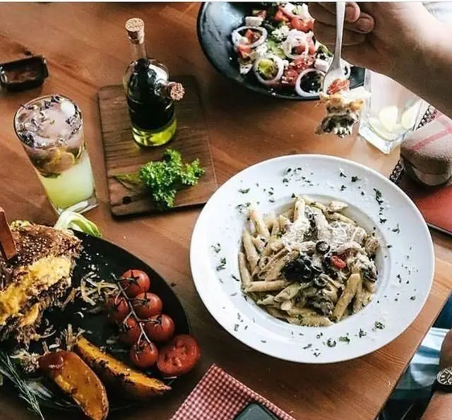 نمایی از میز غذای لذیذ در کافه رستوران پاشا شامل پاستا، سالاد تازه، ساندویچ، سیب زمینی شیرین و نوشیدنی گوارا با فضای دلنشین.