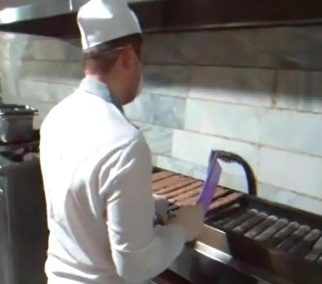 آشپز تهیه غذای مبارکه در حال پخت کباب بر روی گریل در آشپزخانه صنعتی، آماده‌سازی غذای تازه و با کیفیت برای مشتریان.