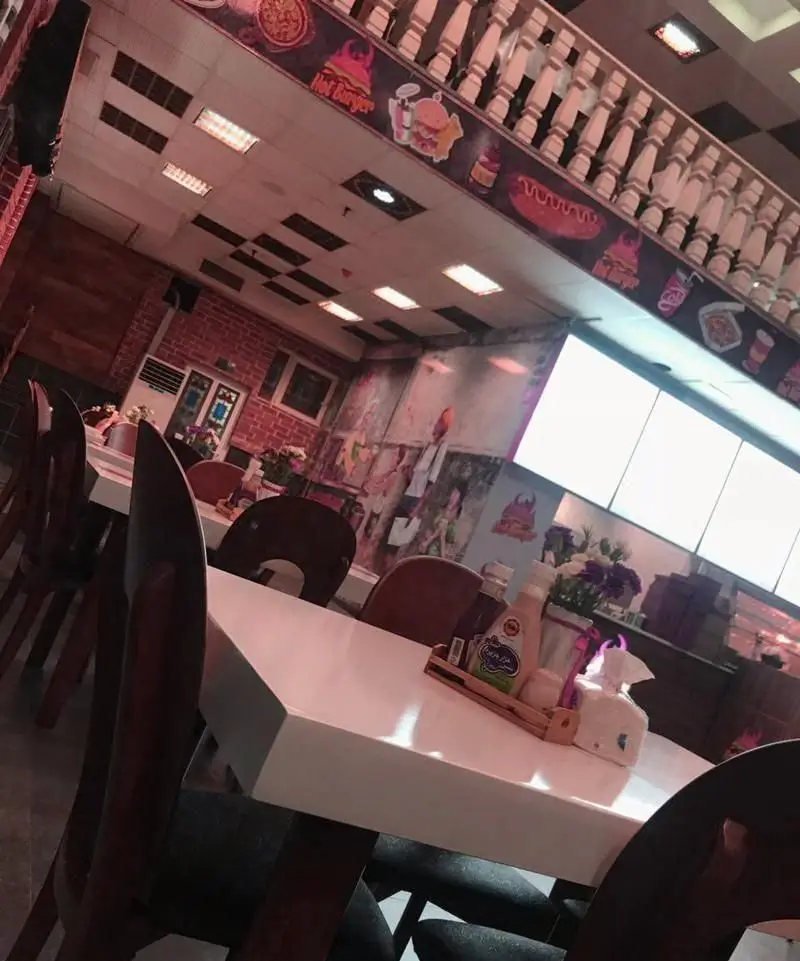 نمایی از فضای داخلی رستوران فست فود هات برگر با دکوراسیون مدرن و تصاویر فست فود روی دیوار، شامل میز و صندلی‌های مرتب برای مشتریان.