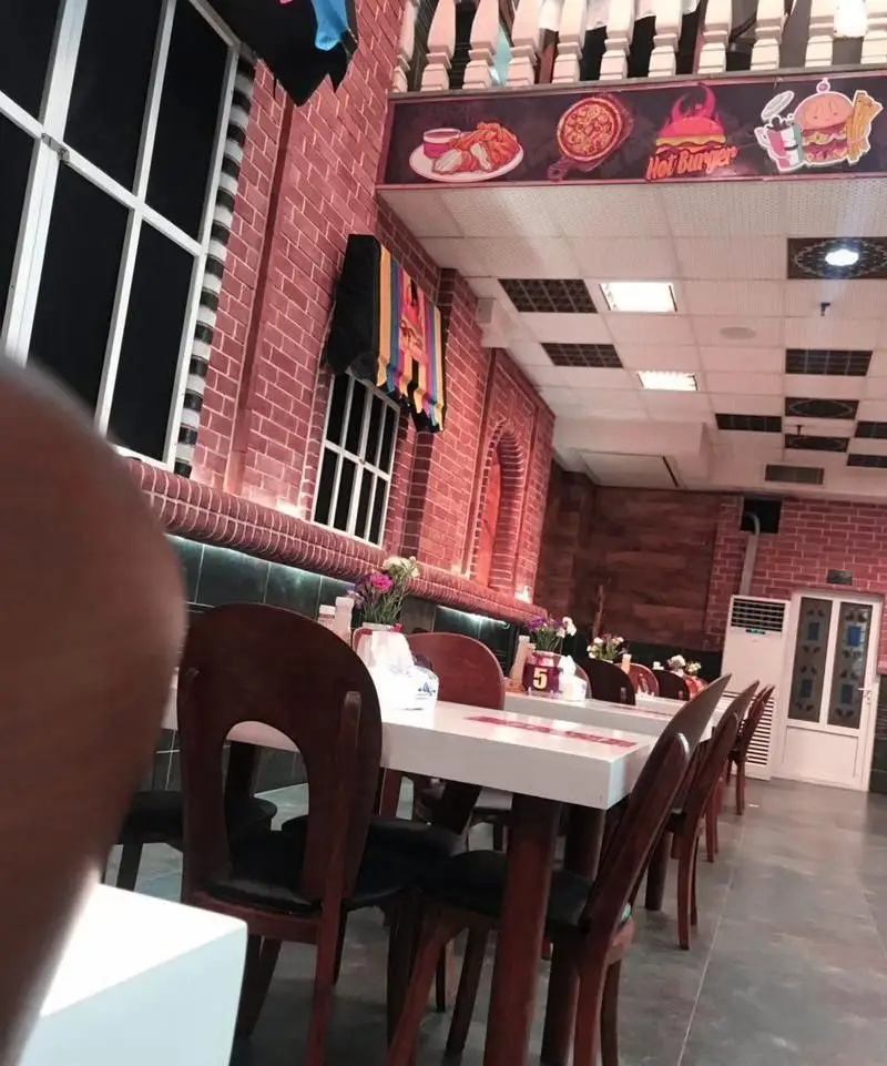 فضای داخلی دنج و مدرن فست فود هات برگر با دیوارهای آجری، میز و صندلی‌های شیک و بنر تبلیغاتی برگر، پیتزا و مرغ سوخاری.