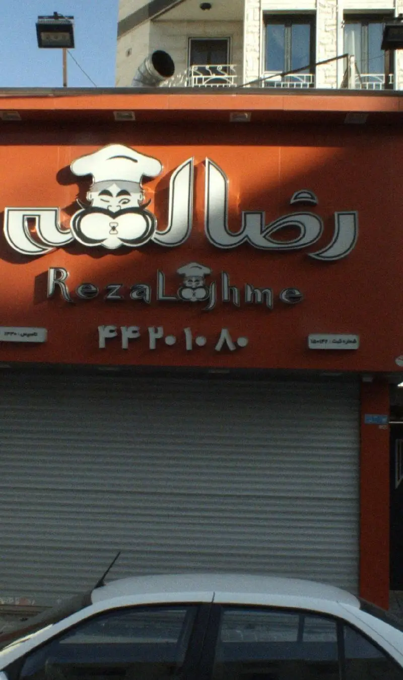 تابلوی بزرگ فست فود رضا لقمه با نماد سرآشپز و سبیل خندان، نمای مغازه بسته با کرکره. شامل تلفن ۴۴۲۰۱۰۸۰ و همبرگوشت ۱۸۰گرمی.