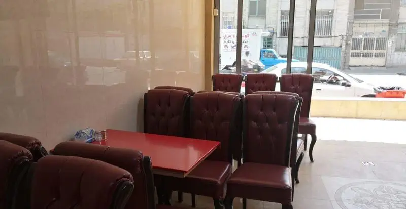 فضای داخلی دنج رستوران رضا لقمه با صندلی‌های زرشکی راحت و میزهای قرمز، نشان‌دهنده غذای تازه شامل گوشت و مرغ.