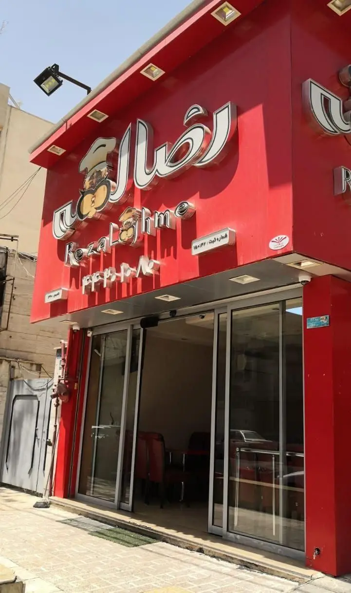 تصویر نمای بیرونی فروشگاه رضا لقمه با سردر قرمز، تابلوی بزرگ و جذاب اسم کسب و کار به فارسی و انگلیسی، و درب شیشه‌ای ورودی.