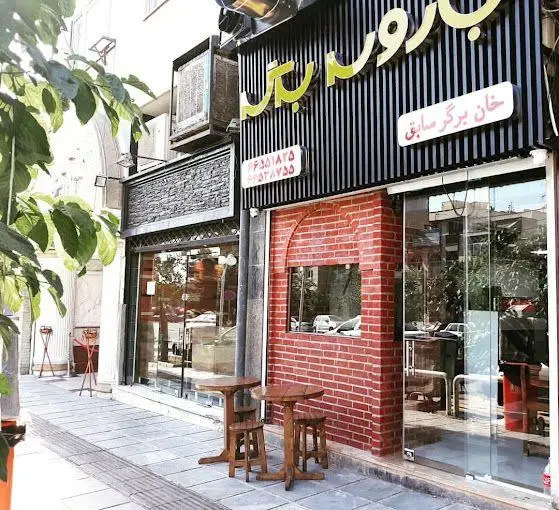 نمای بیرونی فست فود باروس برگر و خان برگر صادق در تهران، شامل میز و صندلی چوبی کنار پیاده‌رو با سردر شیک و آجری.