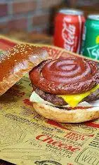 تصویر یک چیزبرگر مخصوص باروس برگر با نان حلزونی قهوه ای، پنیر چدار آب شده و سس ویژه در کنار نوشابه کوکاکولا و اسپرایت. تجربه طعم بی نظیر فست فود.