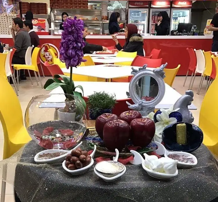 رستوران البیک: سفره هفت سین نوروزی زیبا با سیب، سبزه و آینه، فضایی دلنشین برای مشتریان و جشن‌های بهاری شاد.