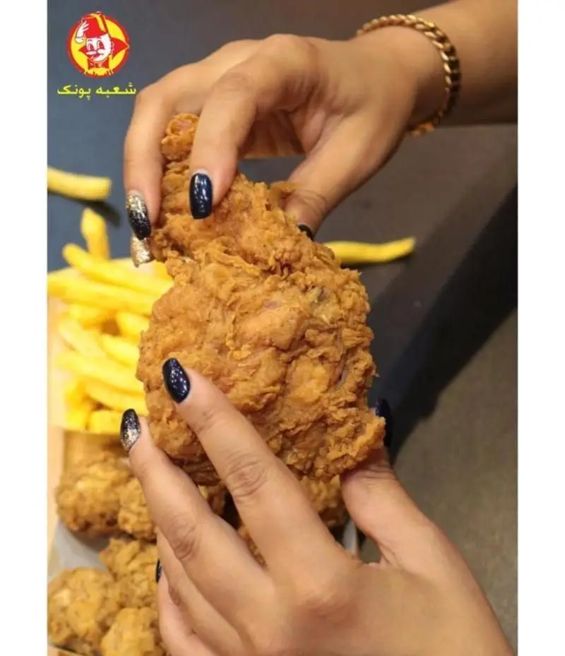 تصویری اشتهاآور از مرغ سوخاری طلایی و ترد رستوران البیک، به همراه سیب زمینی سرخ کرده داغ، در دستان با ناخن‌های زیبا.