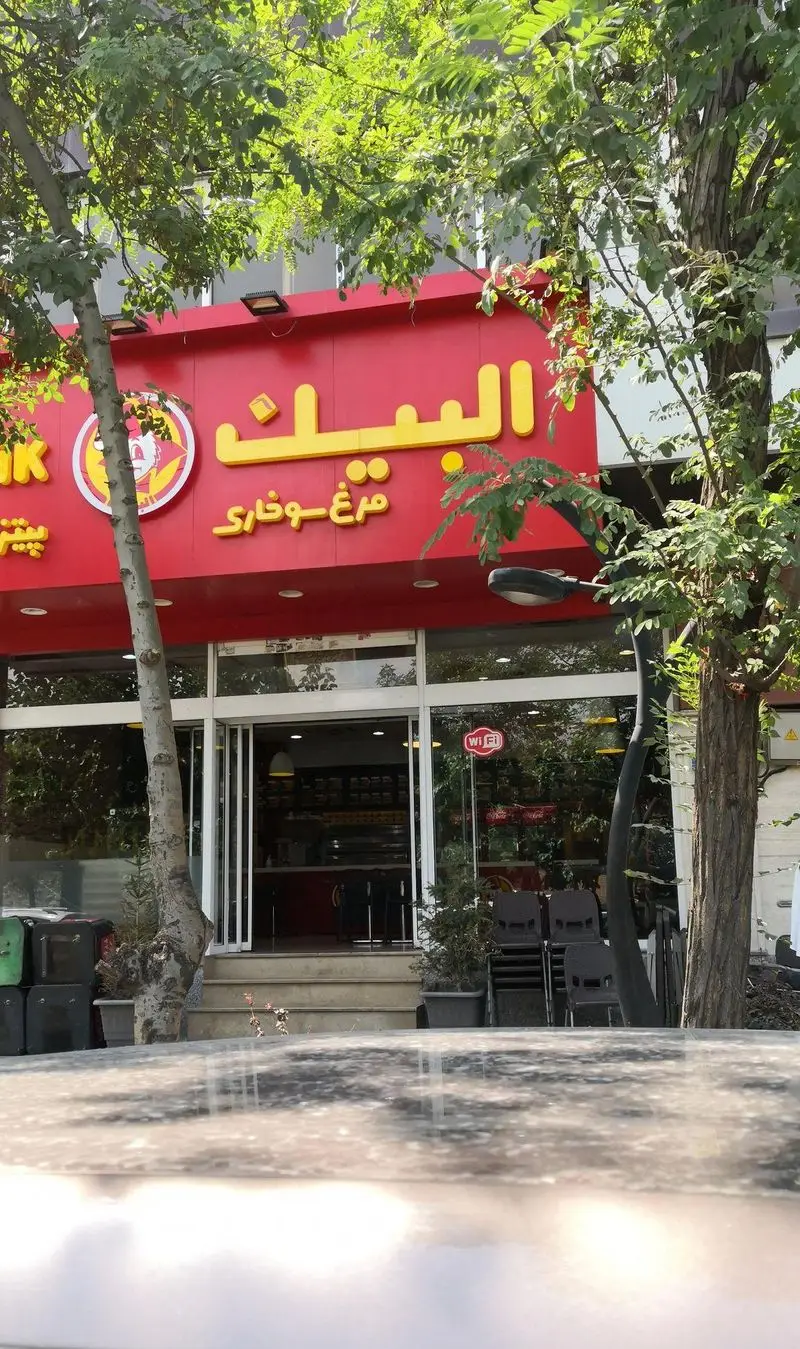 نمای خارجی و ورودی رستوران فست فود البیک، متخصص در مرغ سوخاری، با تابلوی قرمز روشن و حروف زرد "البیک" و لوگوی جوجه معروف.