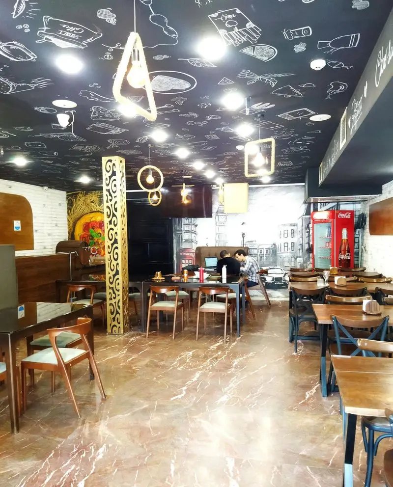 تصویری از فضای داخلی رستوران ایتالیایی ژولی، سقف سیاه با نقاشی‌های جذاب، کف مرمر روشن، میز و صندلی‌های چوبی و مشتریان مشغول گفتگو در فضایی مدرن و گرم.