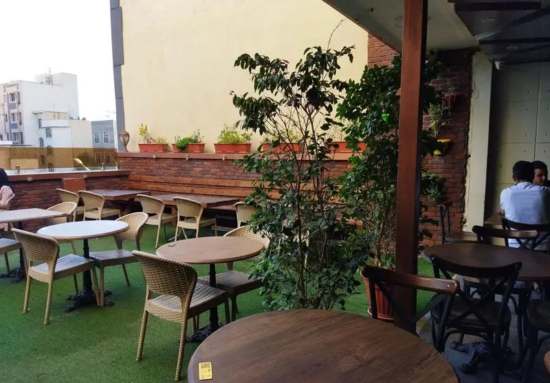 فضای باز و دلنشین رستوران ایتالیایی ژولی با میز و صندلی‌های شیک، کفپوش چمن مصنوعی و گلدان‌های سبز. محیطی عالی برای صرف غذا.