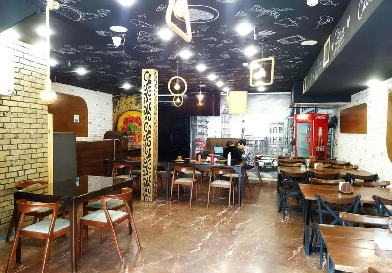 فضای داخلی و دکوراسیون زیبای رستوران ایتالیایی ژولی با سقف سیاه طرح غذا، دیوارنگاره لندن، میز و صندلی چوبی. محیطی دلنشین برای سرو غذا.