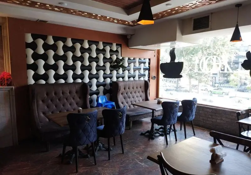 فضای داخلی دنج رستوران ایتالیایی ژولی: دکوراسیون مدرن با دیوار طرح‌دار سیاه و سفید، نیمکت‌های چرمی و صندلی‌های مخمل آبی برای تجربه‌ای دلنشین.