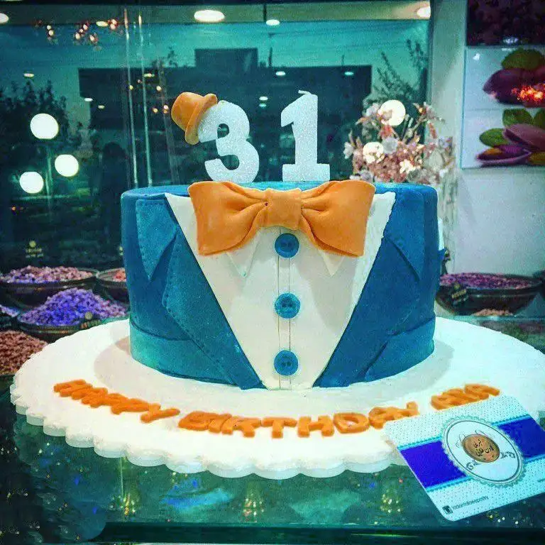 کیک تولد مردانه شیک با طرح کت و شلوار آبی و پاپیون نارنجی، مناسب جشن تولد ۳۱ سالگی از شیرینی لادن طلایی، سفارش آنلاین کیک لاکچری.