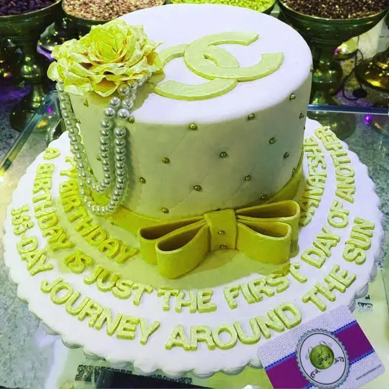 کیک تولد دو طبقه لوکس از شیرینی لادن طلایی، با تزئینات گل رز زرد، مروارید، و متن تبریک خاص. انتخابی شیک برای جشن‌ها.