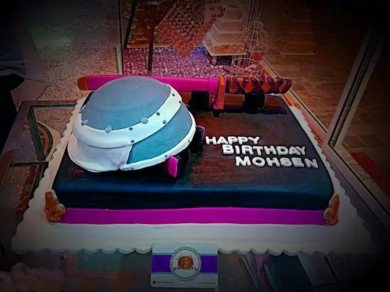 کیک تولد تم خاص مردانه با کلاه خود و شمشیر، طرحی منحصر به فرد روی زمینه مشکی و صورتی. سفارش از شیرینی لادن طلایی.