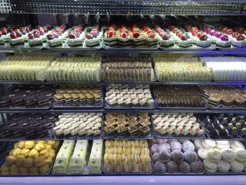 تصویری از ویترین پربار و چشم‌نواز قنادی لادن طلایی شامل ردیف‌هایی از انواع شیرینی‌های تر و خشک، کیک و دسر.