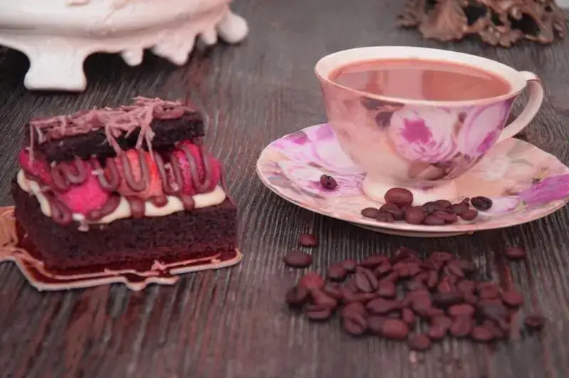 کیک براونی شکلاتی دلپذیر شیرینی لادن طلایی به همراه یک فنجان قهوه داغ معطر و دانه های قهوه روی میز چوبی.