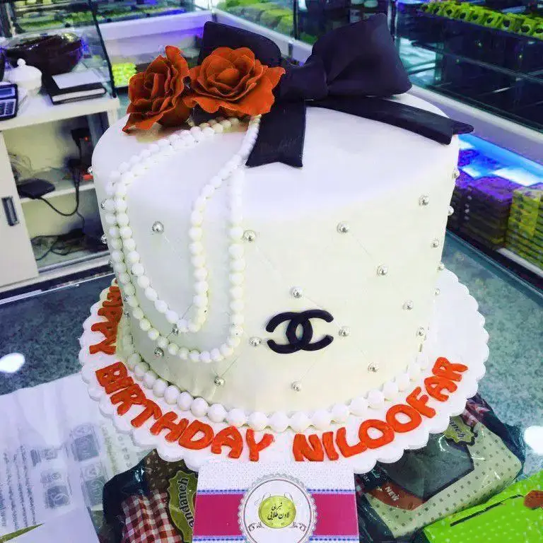 کیک تولد فوندانت زنانه با طرح شنل، مروارید و گل رز نارنجی از شیرینی لادن طلایی، مناسب جشن و مهمانی در تهران.