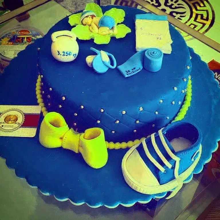 کیک تولد پسرانه آبی با تزیین نوزاد، وزن 3.250 کیلوگرم، تاریخ تولد 16 شهریور و پاپوش‌های نوزادی از شیرینی لادن طلایی