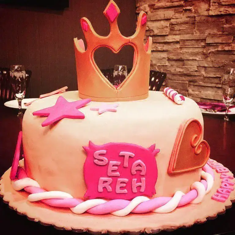 کیک تولد پرنسسی صورتی از شیرینی لادن طلایی با تاج طلایی، ستاره و نام ستاره، مناسب جشن‌های خاص و تولد دخترانه.