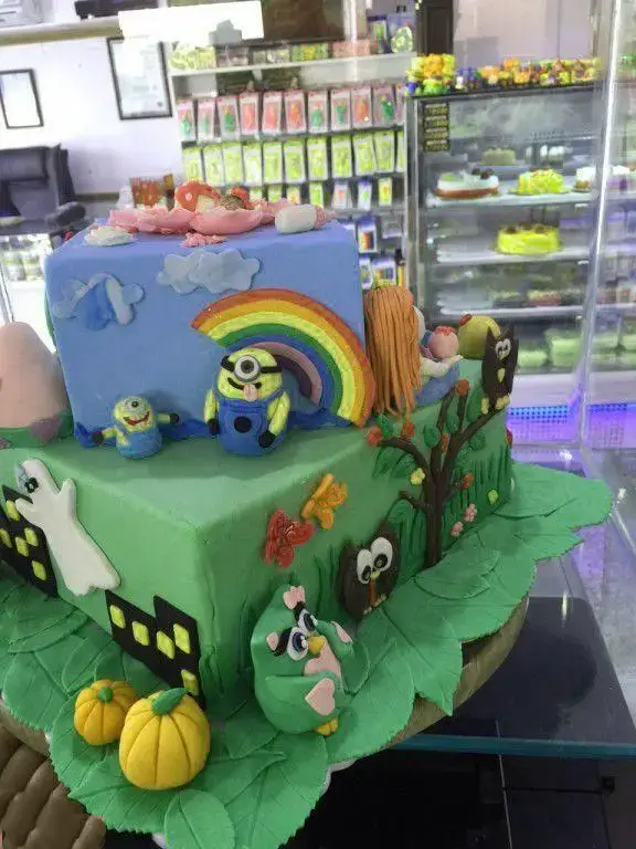 کیک تولد چند طبقه بسیار زیبا و رنگارنگ از شیرینی لادن طلایی با دکور مینیون، پرندگان خشمگین، رنگین‌کمان، روح و کدو حلوایی. مناسب جشن کودکان.