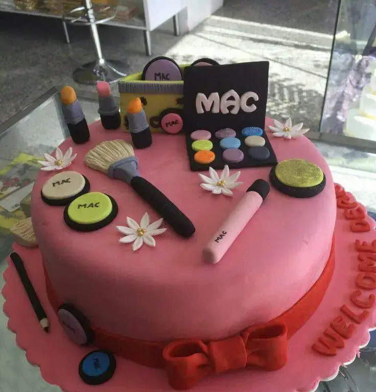 کیک تولد صورتی با دیزاین لوازم آرایشی برند مک شامل رژ لب، پالت سایه، براش و پودر فشرده از شیرینی لادن طلایی.